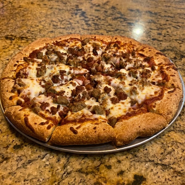 A whole sausage and pepperoni pizza, sliced, on a metal pan atop a granite countertop.