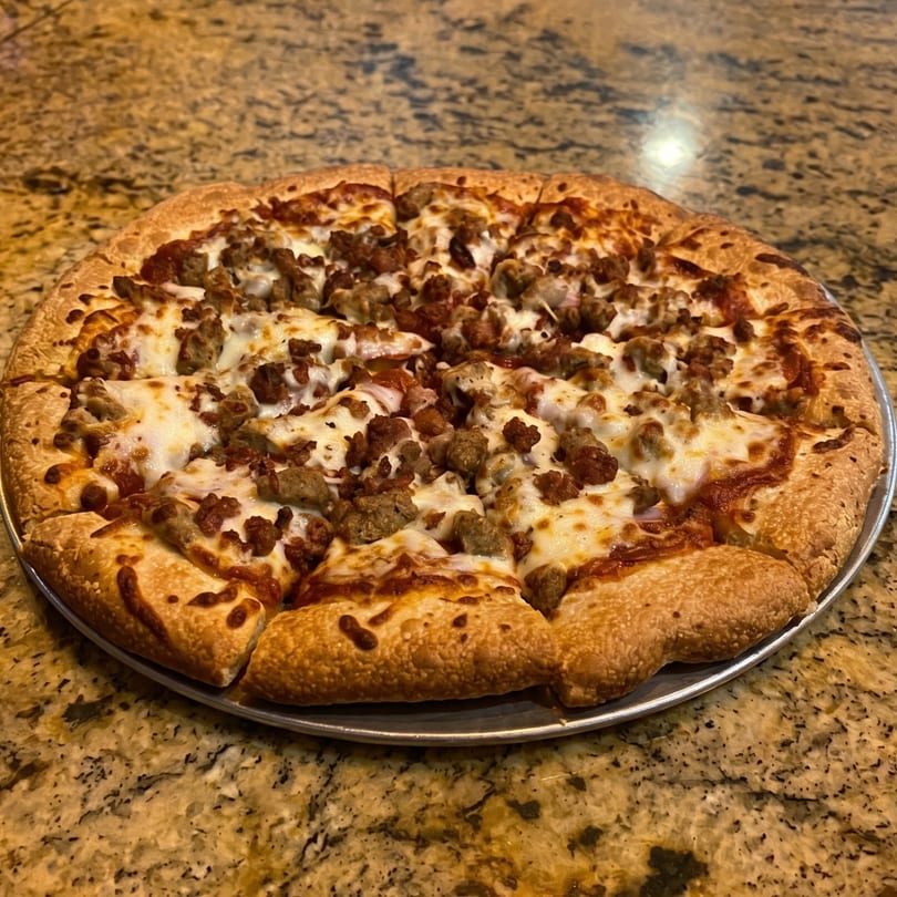 A whole sausage and pepperoni pizza, sliced, on a metal pan atop a granite countertop.