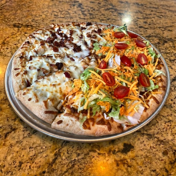 A half bacon chicken ranch, half taco pizza on a metal tray on a granite countertop.