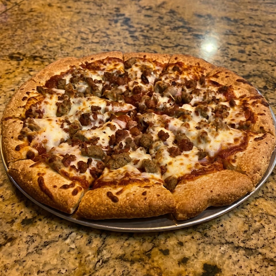 A whole sausage and pepperoni pizza, sliced, on a metal pan atop a granite counter.