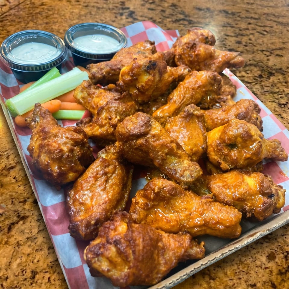 A tray of buffalo chicken wings with celery, carrots, and two cups of ranch dressing.