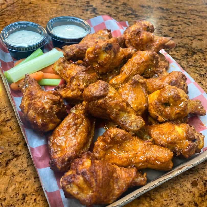 A tray of buffalo chicken wings with celery, carrots, and two cups of ranch dressing.