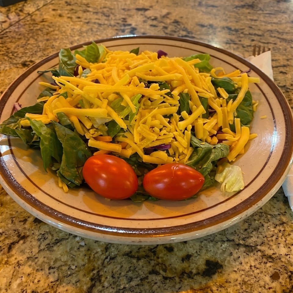 A fresh green salad topped with shredded cheddar cheese and two bright red cherry tomatoes.