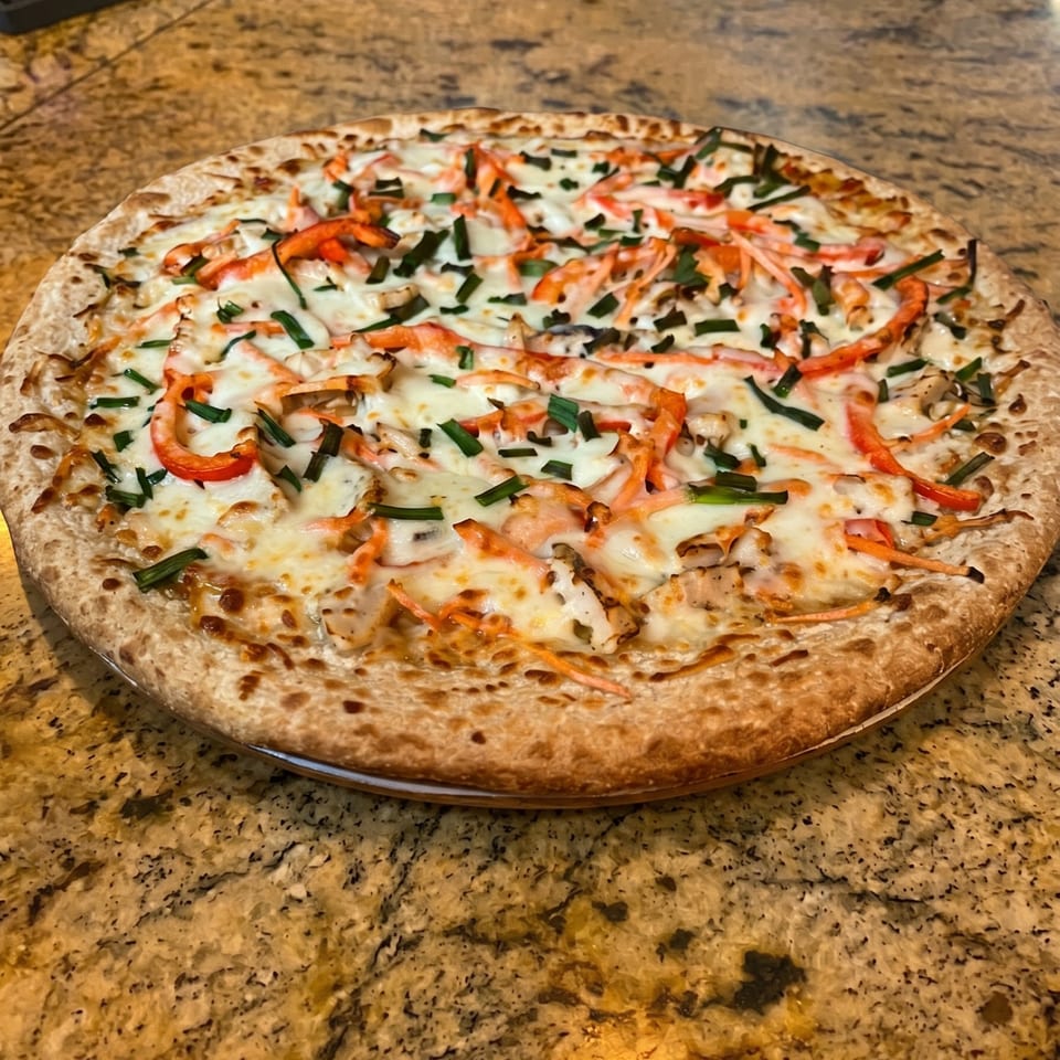 A whole pizza with white sauce, melted cheese, red bell peppers, and chives on a counter.