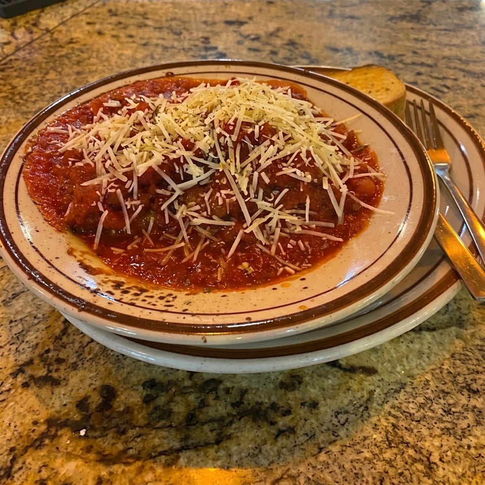 A plate of meatballs and sauce, topped with shredded cheese, next to garlic bread and a fork.