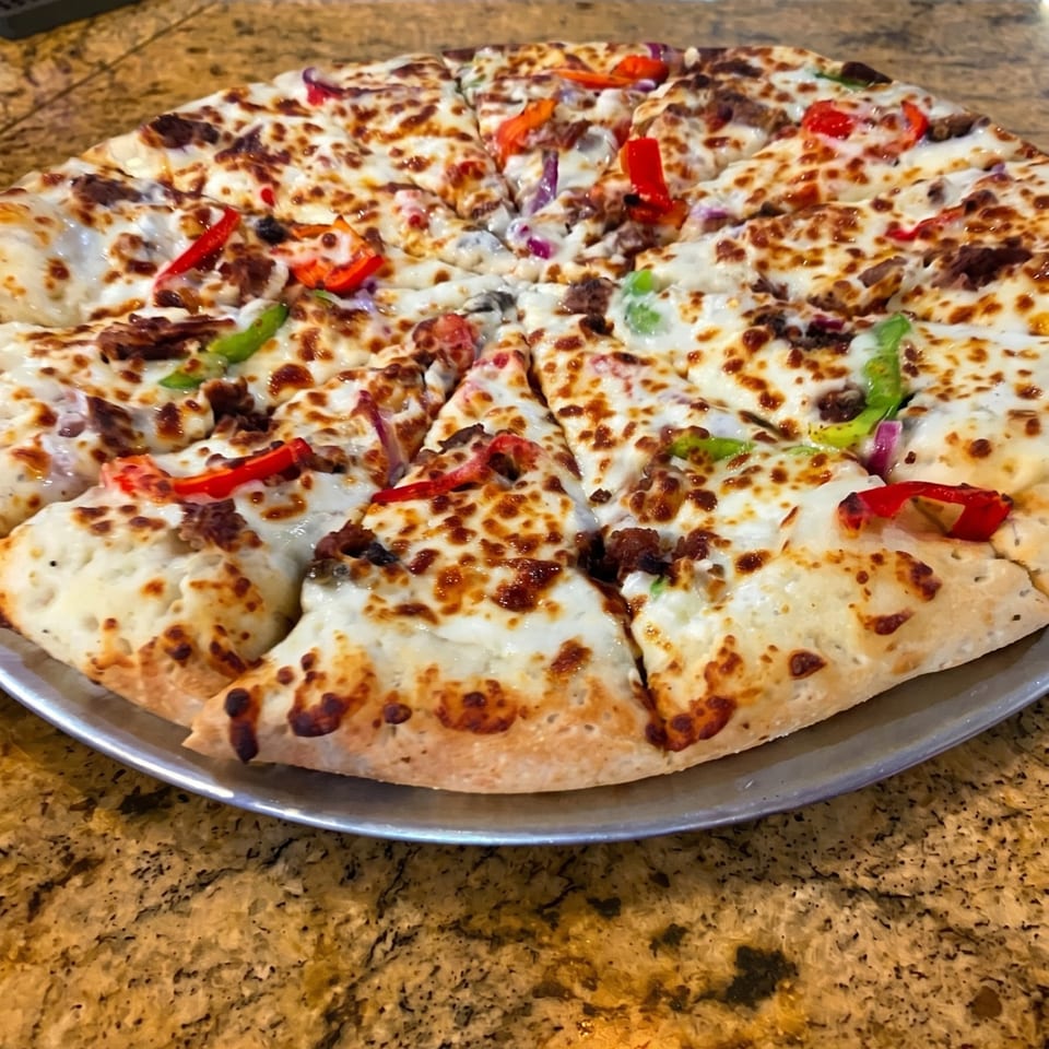 A whole pizza with melted cheese, red and green bell peppers, and red onions on a metal tray.