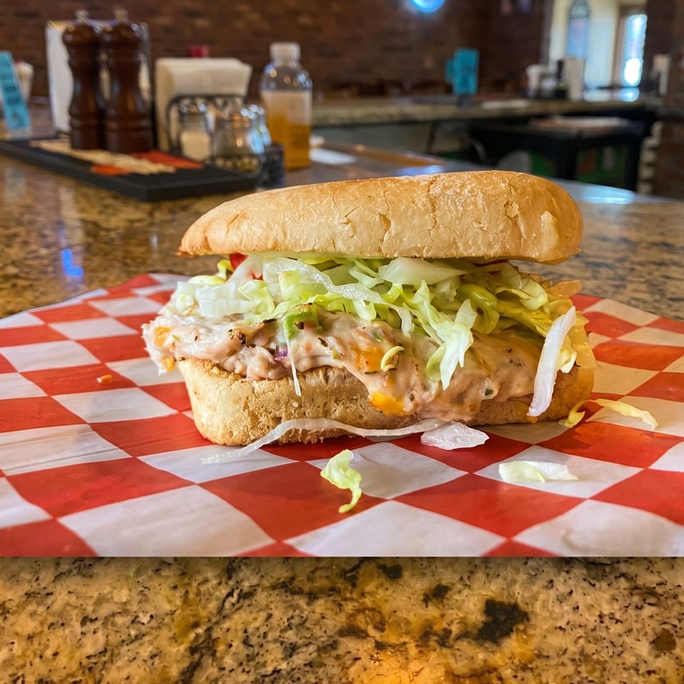 A shrimp po'boy sandwich with lettuce and sauce on red and white checkered paper.