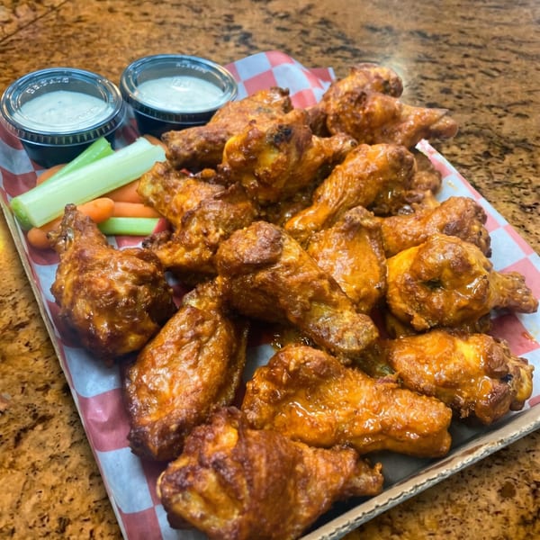 A tray of buffalo chicken wings with celery, carrots, and two dipping sauces.